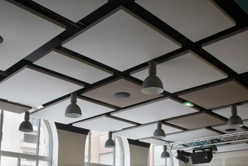 White acoustic ceiling panels suspended in a black grid with integrated lighting